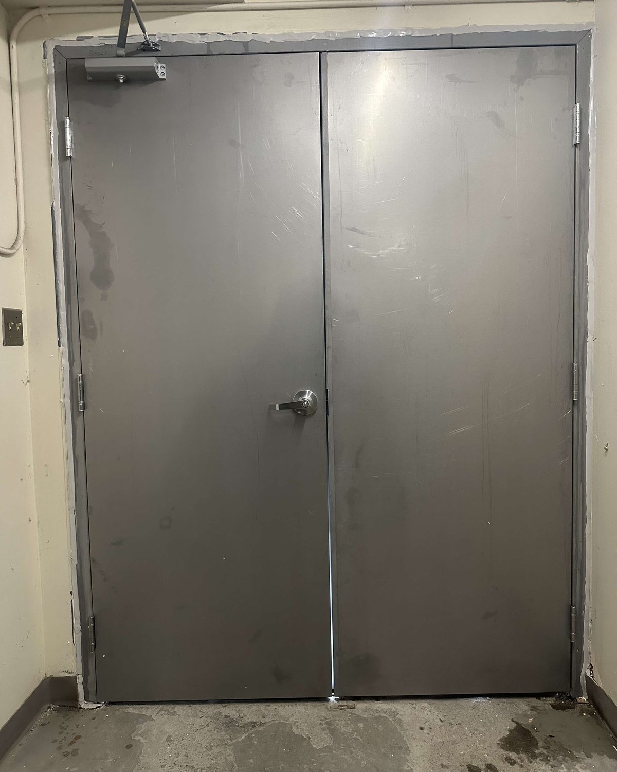 A pair of hollow metal doors on butt hinges in a painted steel frame in a finished corridor, installed by Canuck Door Systems