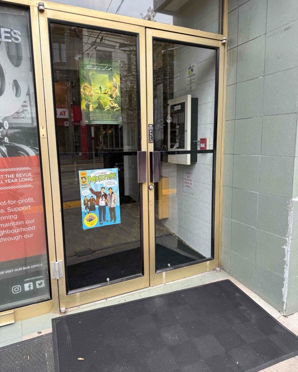 A pair of glazed aluminum entrance doors with posters behind the glass at a cinema storefront, glazed by Canuck Door Systems