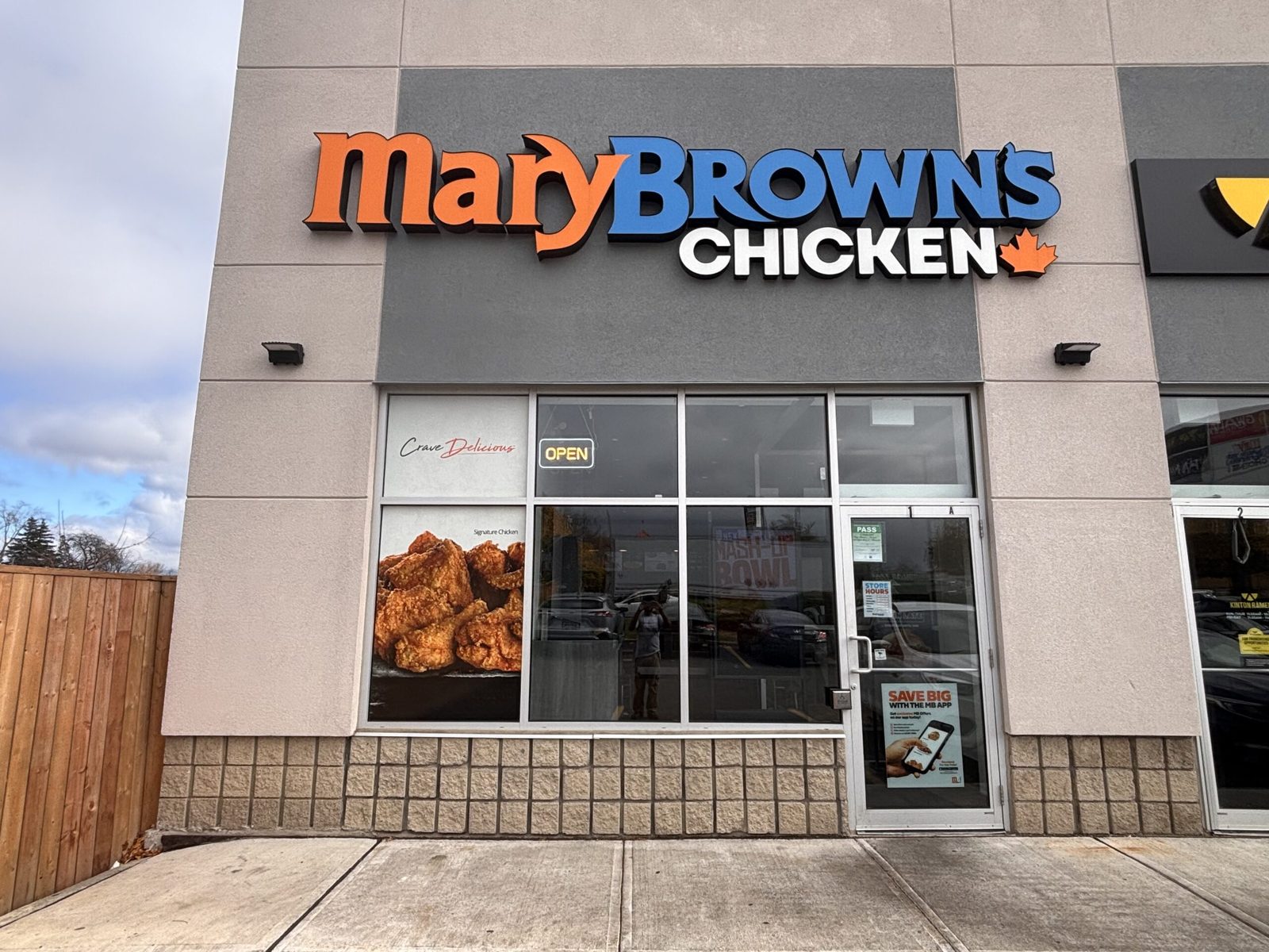 An aluminum-framed storefront with fixed glazing and a narrow-stile glass entrance door at a quick-service restaurant unit in a retail plaza, installed by Canuck Door Systems