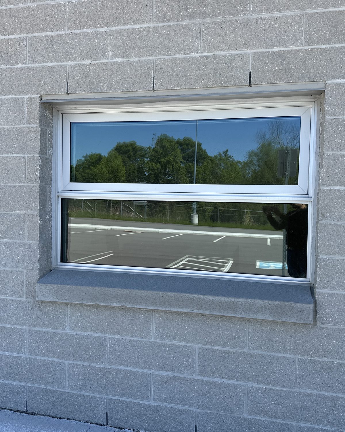 A new aluminum-framed window with tinted glazing and a horizontal slider, set into a concrete block wall, installed by Canuck Door Systems