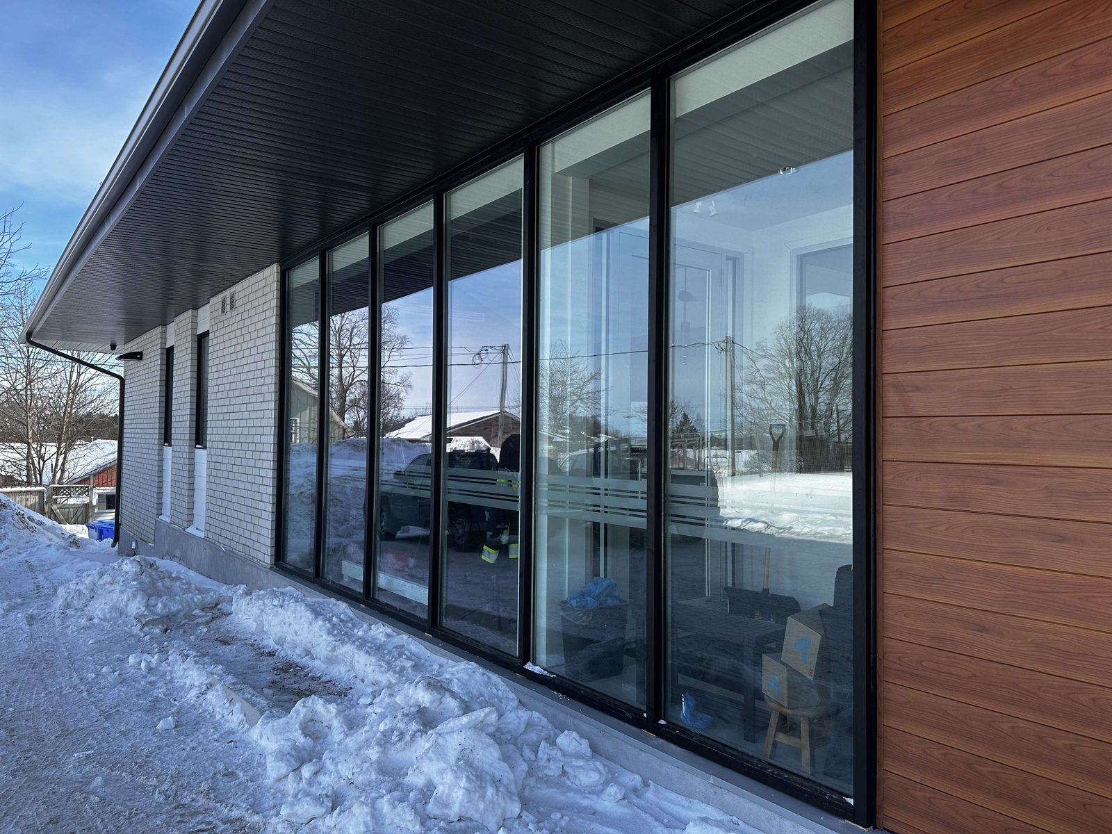 A long run of aluminum-framed commercial windows in a dark elevation beside wood cladding, supplied and installed by Canuck Door Systems