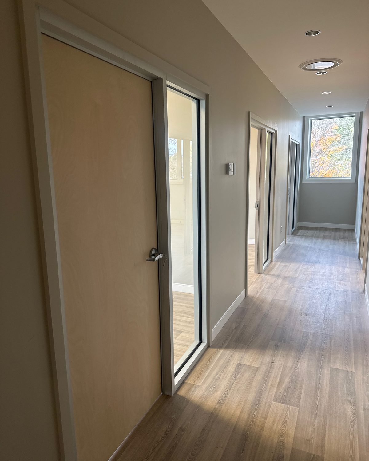 A veneer wood door beside a glazed screen in an office corridor, installed by Canuck Door Systems