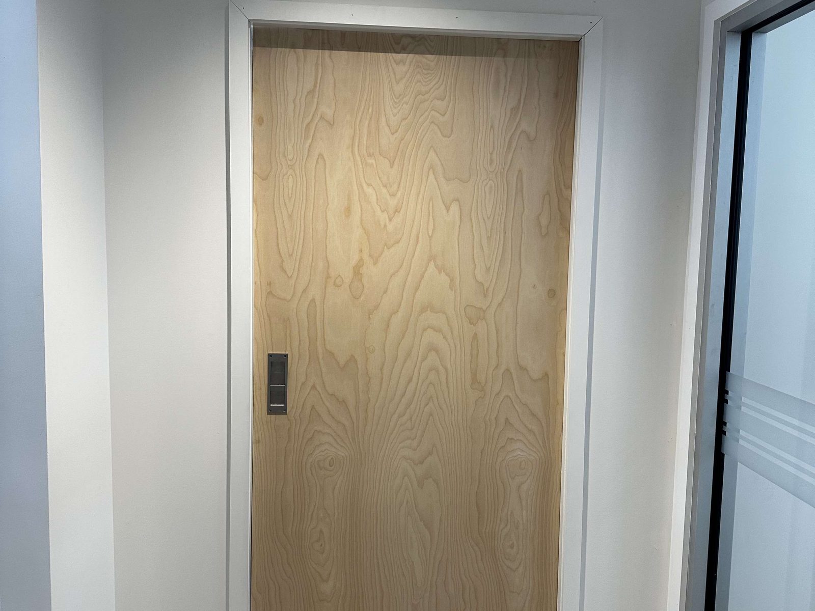 A wood-veneer door leaf with a recessed flush pull, hung in a painted frame in a finished interior, installed by Canuck Door Systems