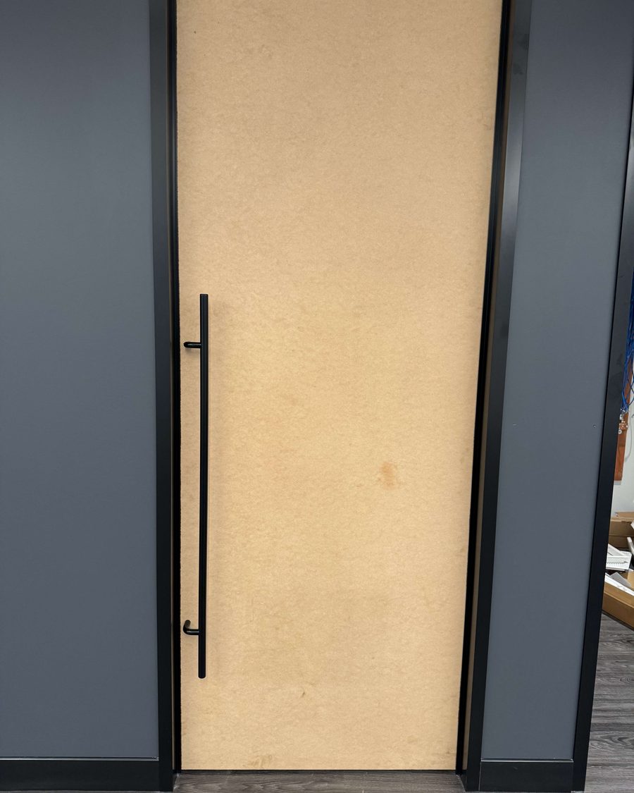 A pair of light veneer commercial doors with long black pulls in a dark painted frame, installed by Canuck Door Systems