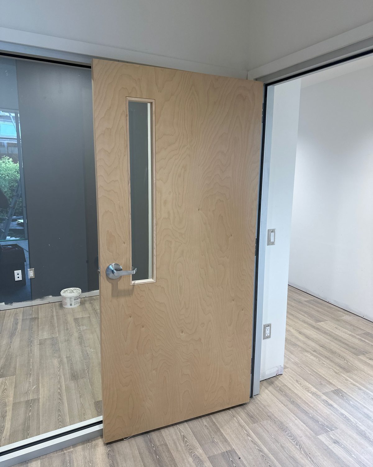 A wood-veneer door with a full-height narrow vision lite in a finished corridor, installed by Canuck Door Systems
