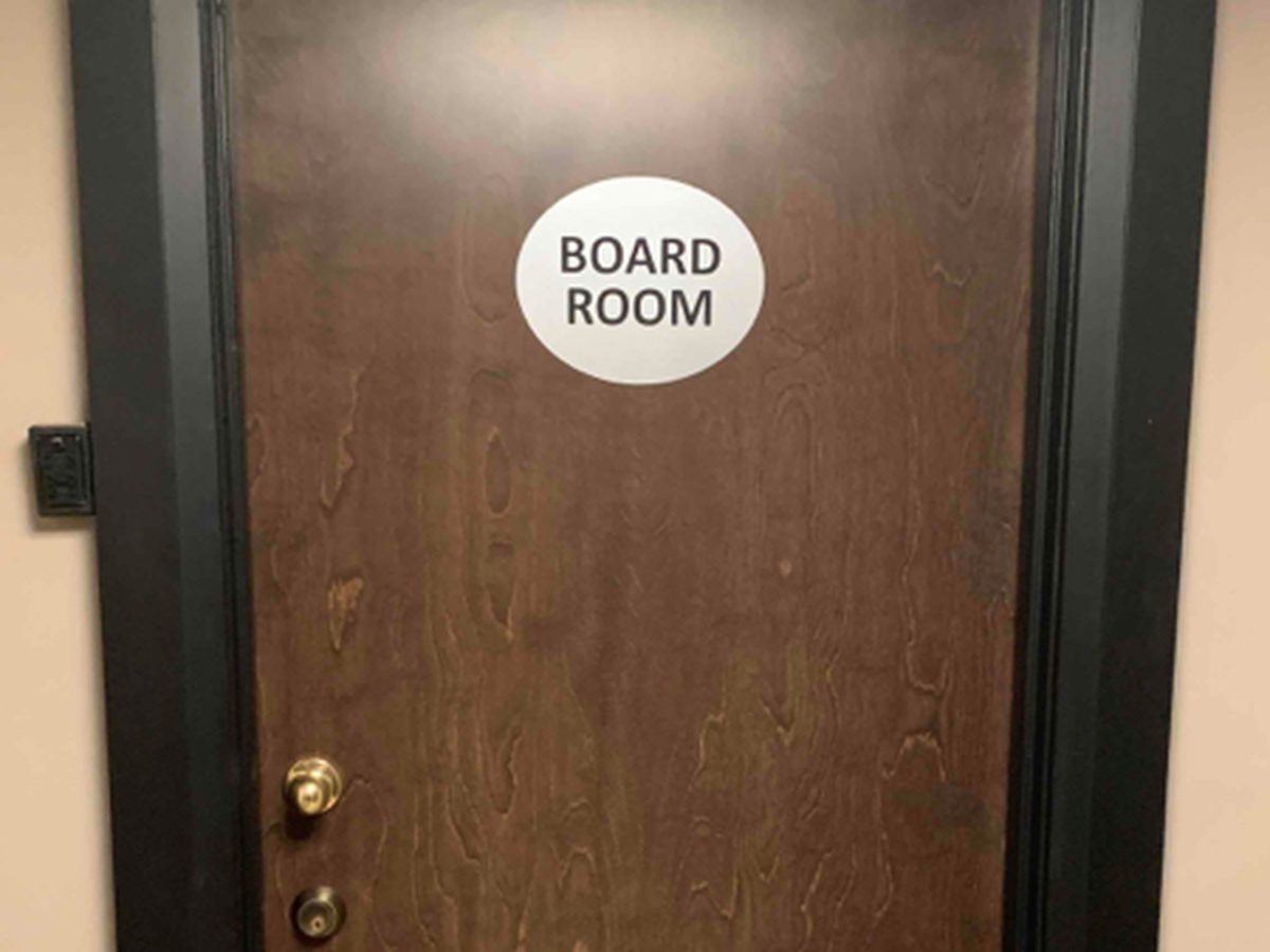 A dark-stained wood-veneer boardroom door with a BOARD ROOM sign, hung in a painted steel frame, installed by Canuck Door Systems