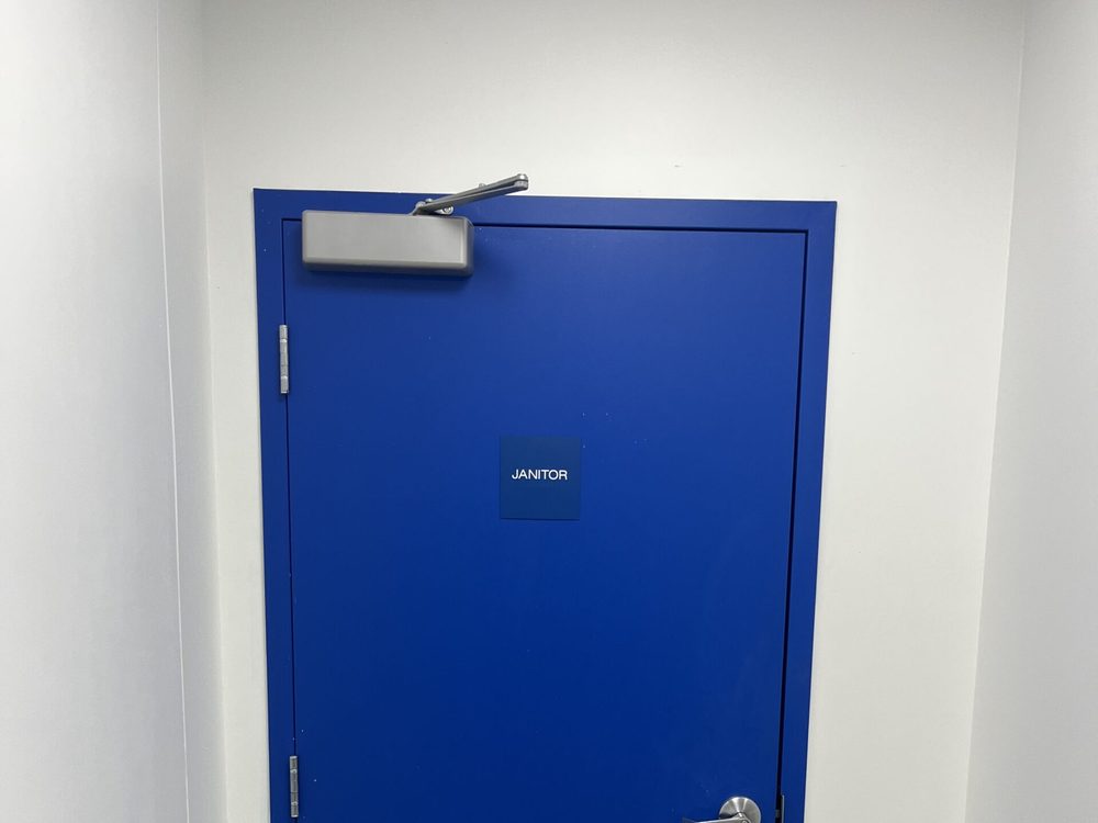 A blue-painted hollow metal janitor door in a welded steel frame with a surface door closer, installed by Canuck Door Systems