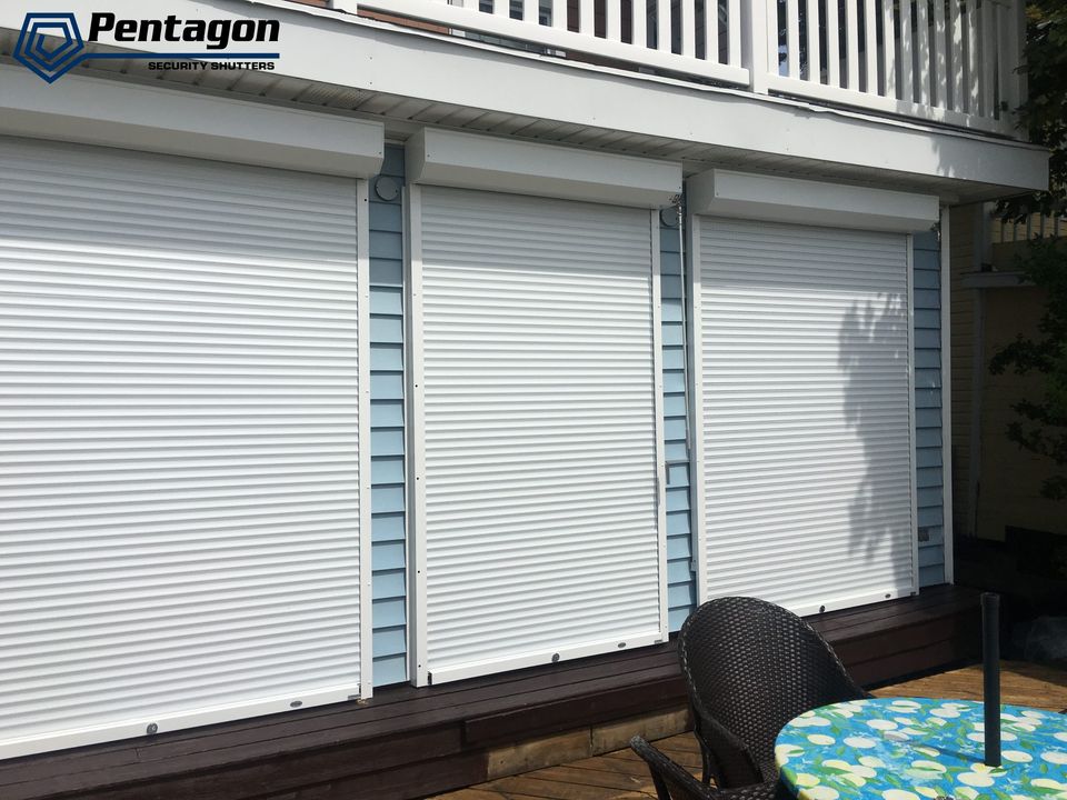 White rolling shutters lowered over the windows of a house with blue siding