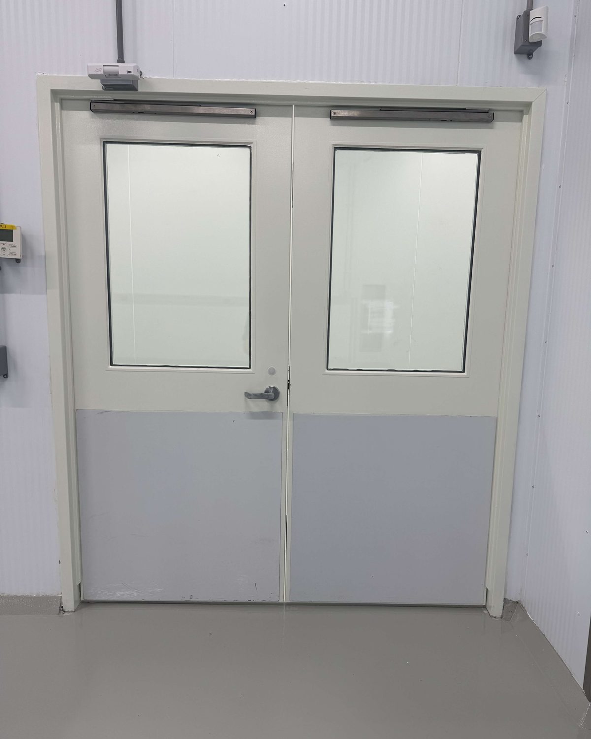 A pair of white hollow metal doors with large vision lites and kick panels, in a steel frame, inside Curaleaf's facility in Brampton