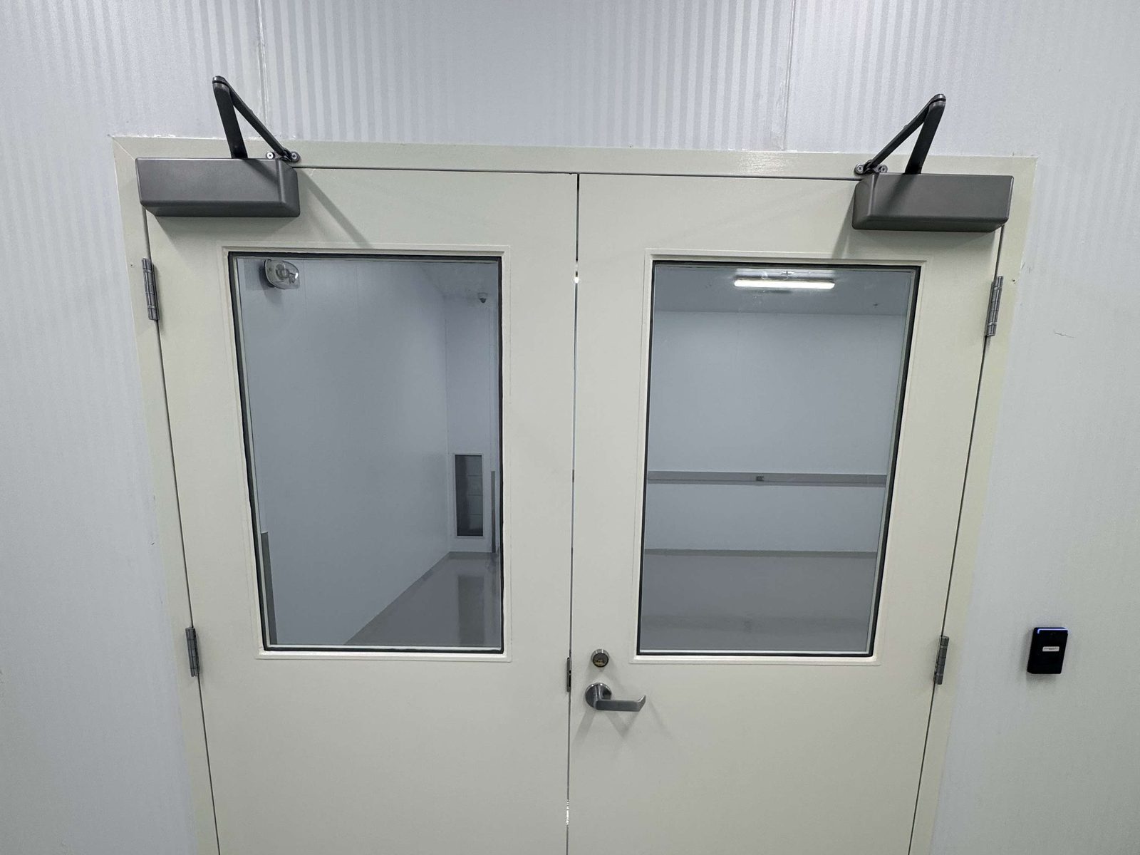 A pair of white hollow metal doors with vision lites and overhead closers in a welded steel frame, inside Curaleaf's facility in Brampton, installed by Canuck Door Systems