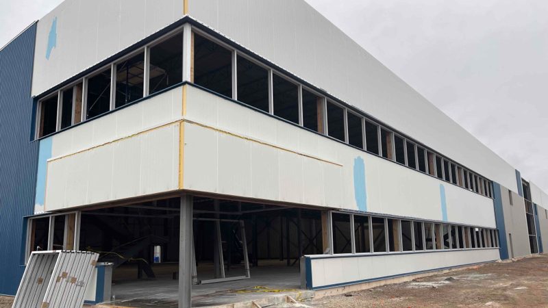 The Metelix expansion in Brampton under construction, with aluminum window frames set in the upper-floor openings before glazing and the ground floor still open to the steel structure