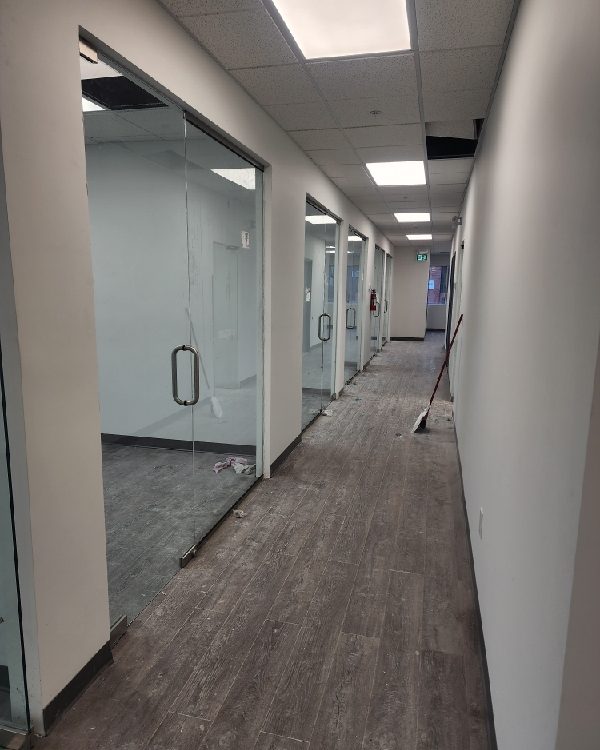 An office corridor lined with frameless glass walls and glass doors with pull handles, before the final clean-up