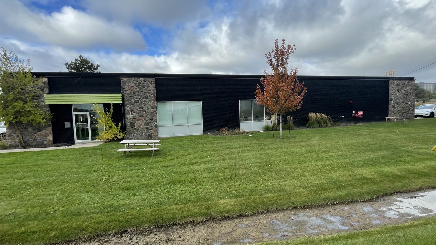 The end of one of the Kelfield Street buildings in Etobicoke, a low commercial building with a stone pier, a glazed entrance and new windows, seen across a lawn