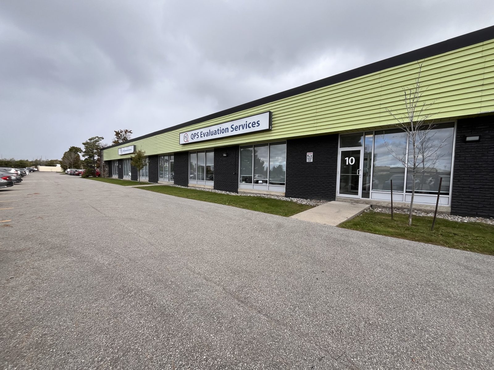 A long single-storey row of commercial units at Kelfield Street in Etobicoke, with new aluminum storefronts and windows below a green fascia band, installed by Canuck Door Systems