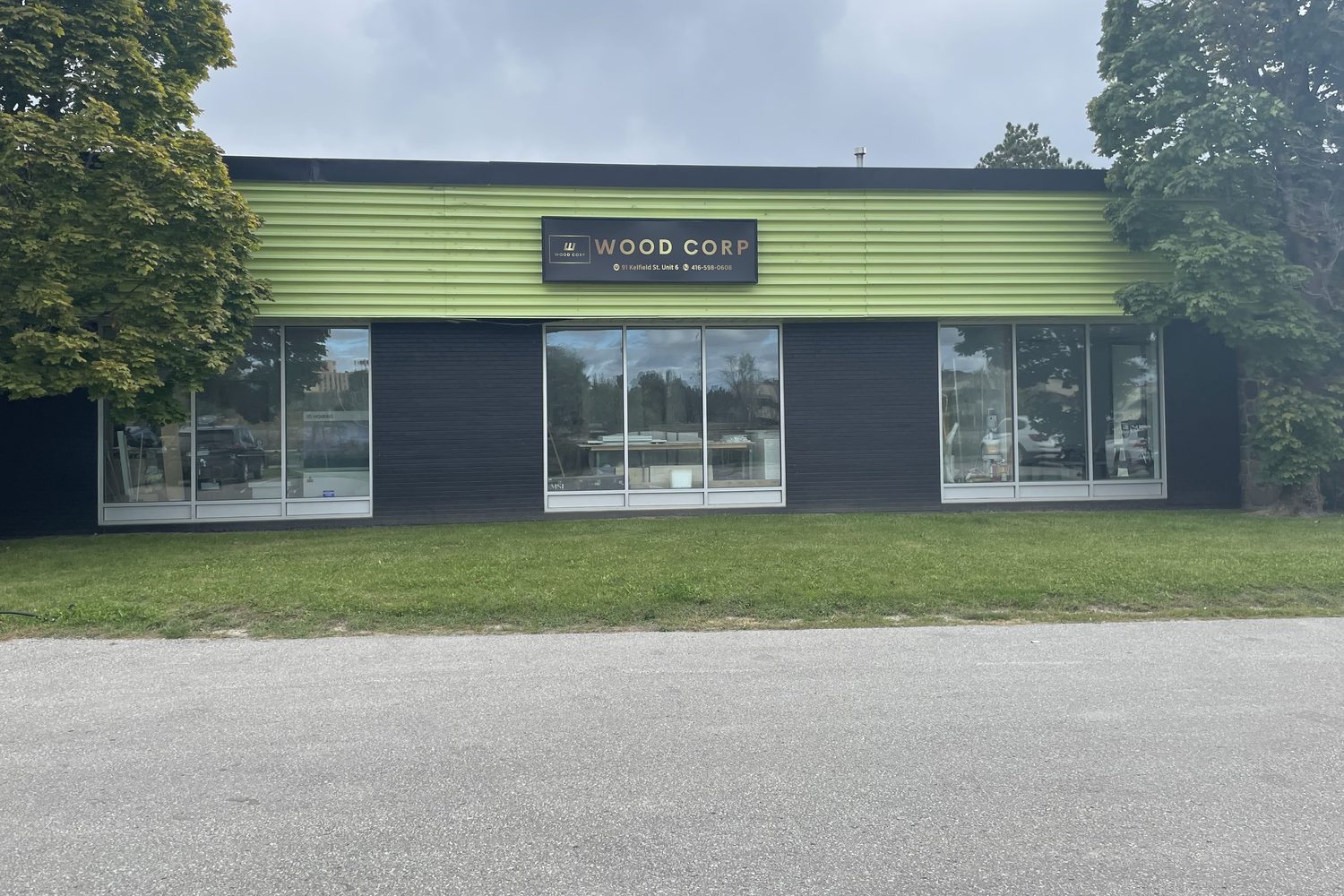 Three wide new aluminum storefront windows under a green fascia band on a commercial unit at Kelfield Street in Etobicoke, with trees either side