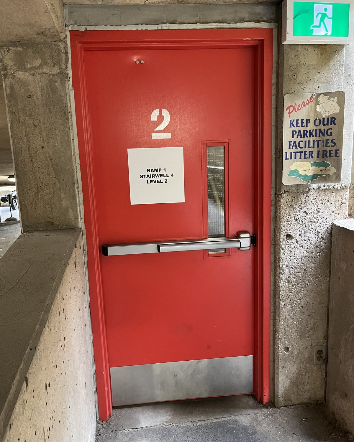 A red hollow metal stairwell door with a panic bar and a large number 2, set in a concrete wall of the St. Joseph's Healthcare Hamilton parking garage