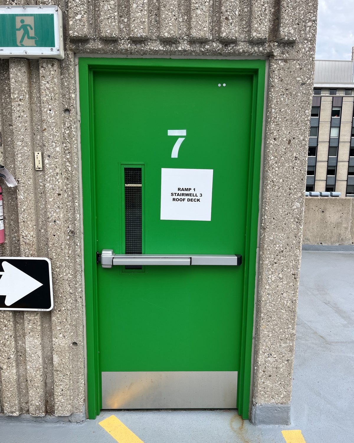A green hollow metal stairwell door with a panic bar and a large number 7, in the St. Joseph's Healthcare Hamilton parking garage