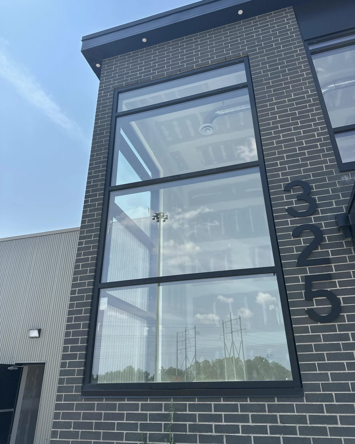 A tall black-framed aluminum window running the full height of a dark brick office front in Hamilton, divided into four lites, with the address numerals 325 mounted on the brick beside it