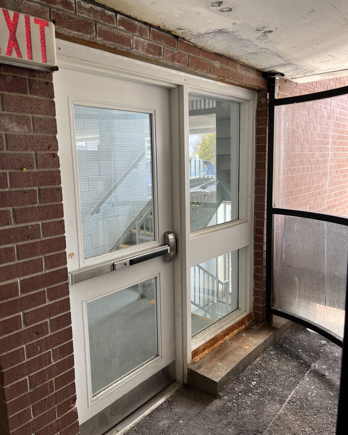 A white hollow metal door with a vision lite beside a glazed sidelite, set in a brick wall in the Grand River Hospital parking garage in Kitchener