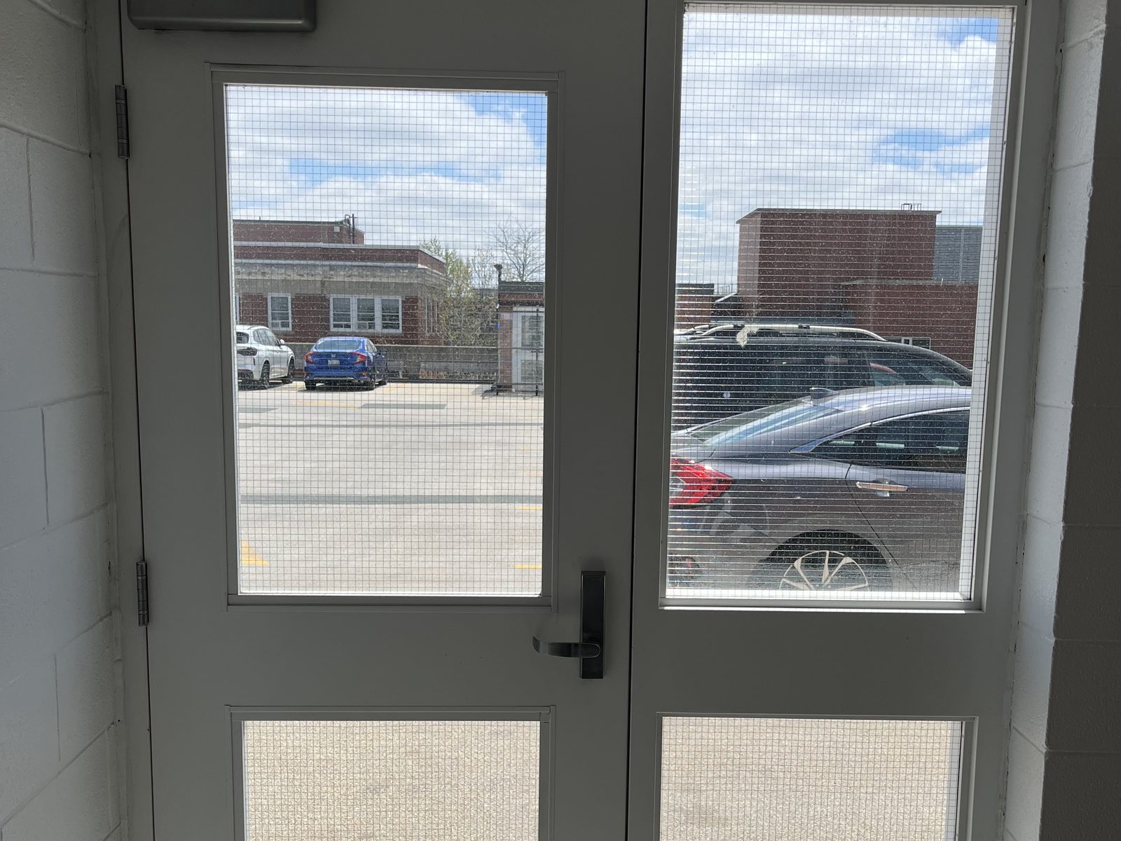 A pair of new white hollow metal doors with large vision lites and a panic bar, in a welded frame at a stairwell in the Grand River Hospital parking garage in Kitchener, installed by Canuck Door Systems