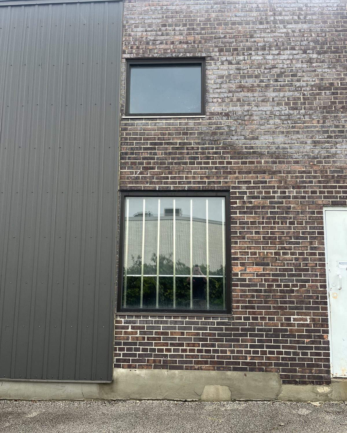 A new aluminum-framed window in the brick wall of Sable Metal Fabrication in Markham, beside a section of dark metal cladding