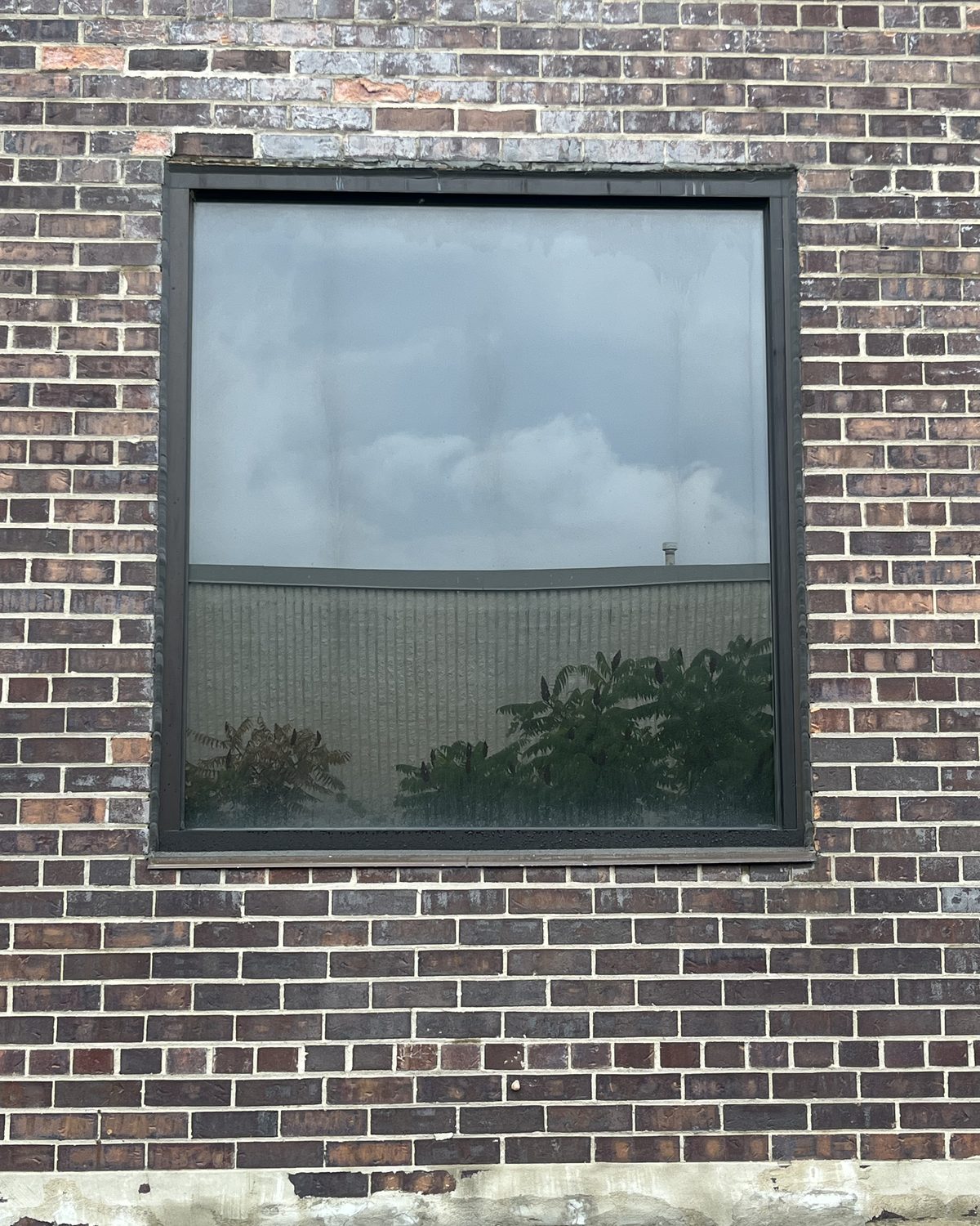 A large square aluminum-framed window with bronze tinted glass set into the dark brick wall of Sable Metal Fabrication in Markham