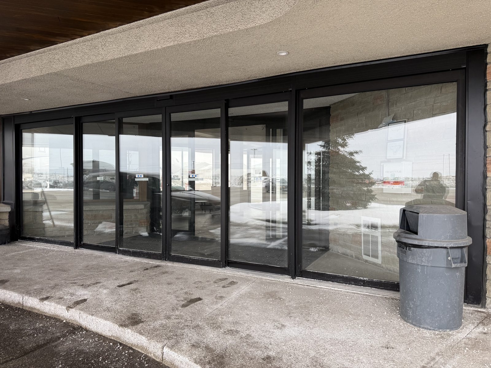 A run of dark aluminum-framed automatic sliding doors and glass panels under a curved concrete canopy at Signature Aviation in Mississauga, installed by Canuck Door Systems