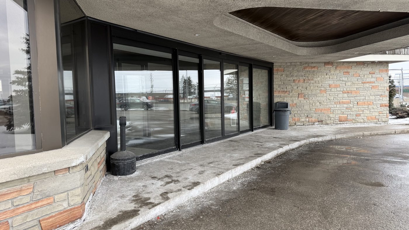 The entrance at Signature Aviation in Mississauga seen along the curved walkway under the concrete canopy, with the new glazed sliding doors set into the stone base