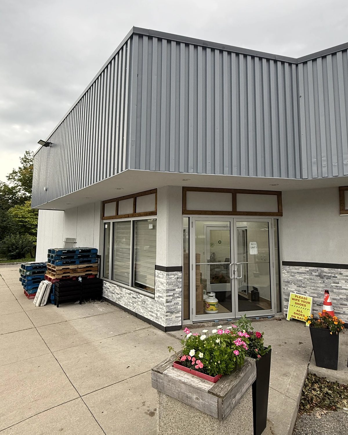The end unit of the Mississauga plaza, with new aluminum storefront windows and double doors under the grey metal fascia, planters at the entrance