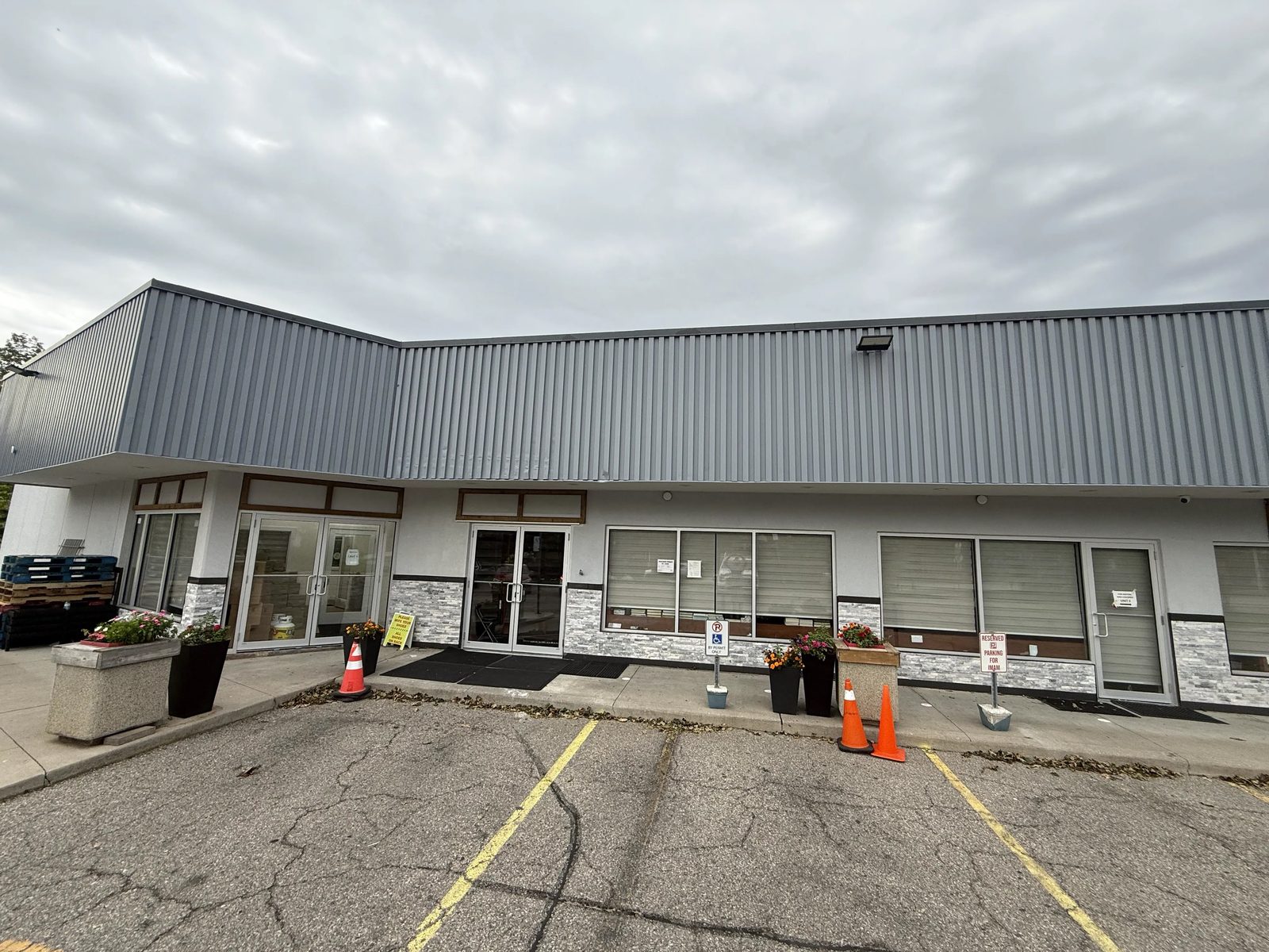The corner of the plaza at 6120 Montevideo Road, Mississauga, with new clear anodized aluminum storefront doors and windows set into white stucco and stone veneer under a grey metal fascia, replaced by Canuck Door Systems
