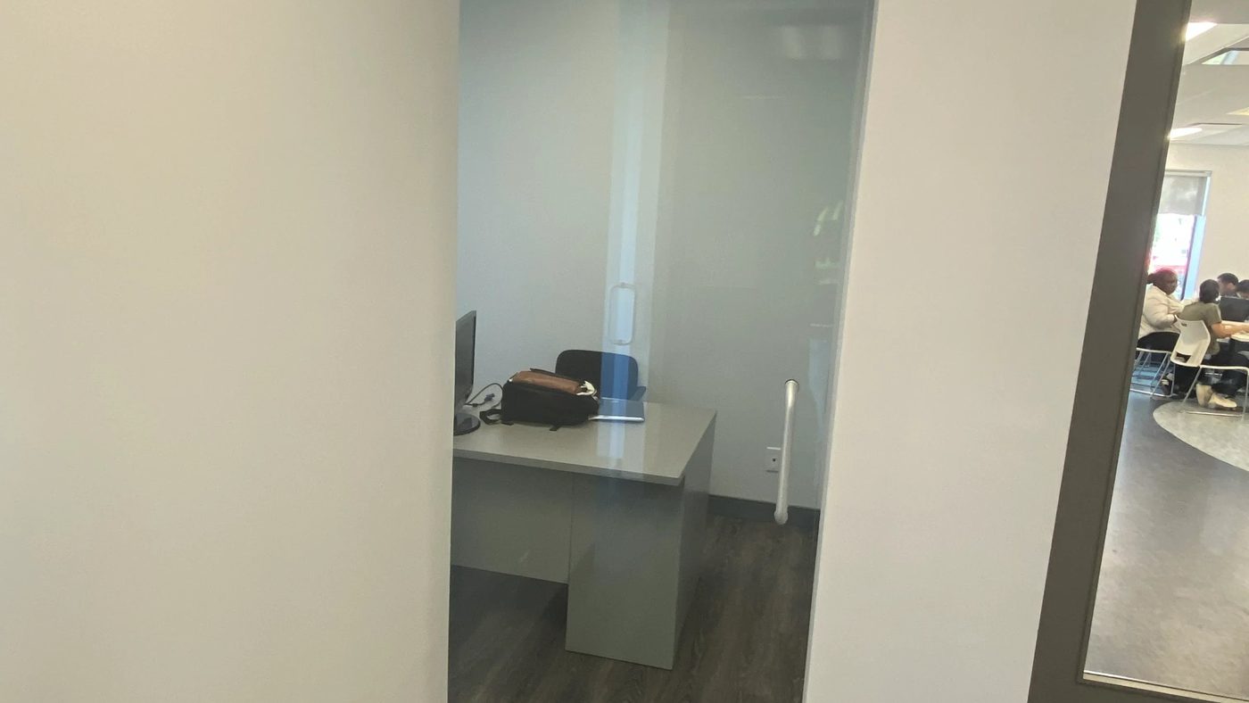 An interior frameless sliding glass door on CRL 690 series hardware closed across an office opening at a Mississauga laboratory, with the open-plan lunchroom beyond, installed by Canuck Door Systems