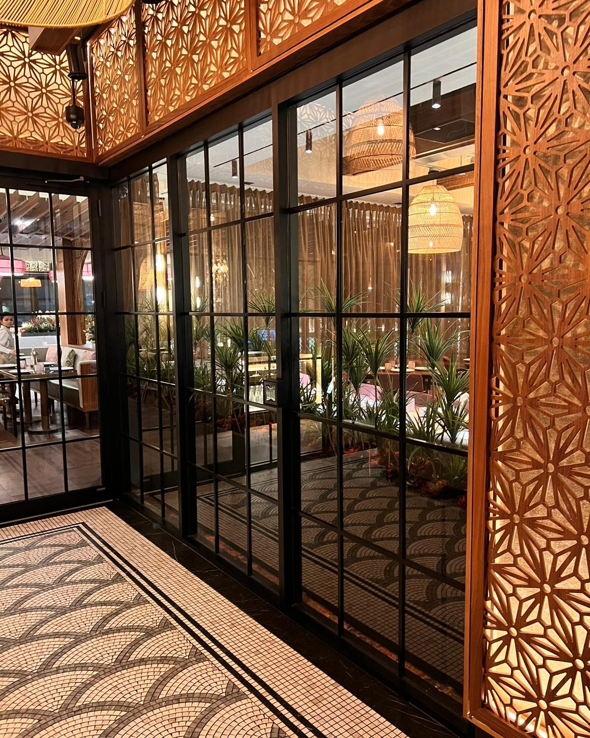 Inside the Mishree restaurant in Mississauga: a wall of dark-framed glass panels seen from inside, beside a carved wood screen