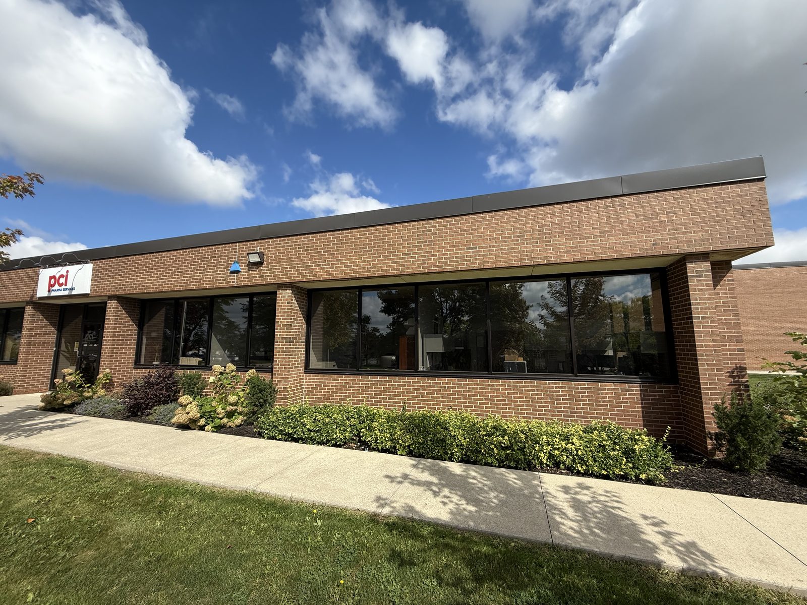 The front of PCI Pharma Services' single-storey brick building in Mississauga, with long bands of new dark-framed aluminum windows along the facade, replaced by Canuck Door Systems