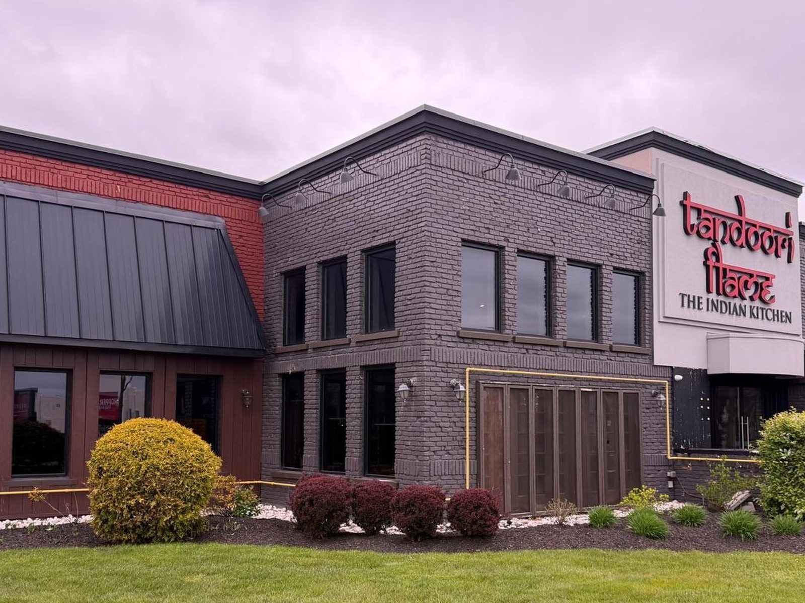 The front of the Tandoori Flame restaurant in Mississauga, a two-storey building with rows of new dark-framed aluminum windows on both floors under a standing-seam metal mansard, replaced by Canuck Door Systems