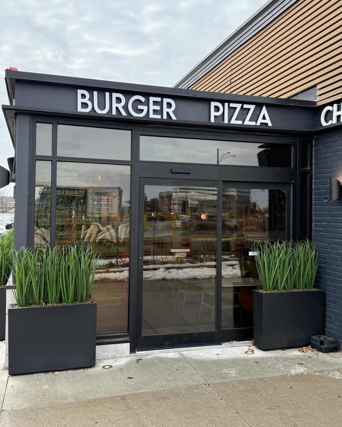 A glazed aluminum entrance on the Happy Singh restaurant in Mississauga, framed in dark aluminum under the restaurant's menu lettering, with tall planters either side
