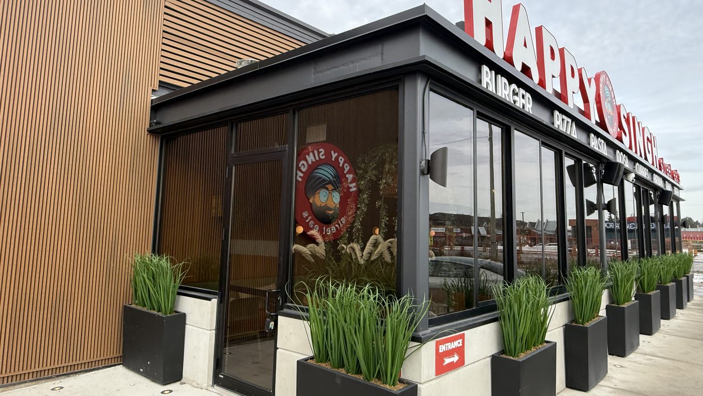 The corner of the Happy Singh restaurant in Mississauga, where the dark aluminum storefront glazing wraps around the building under the restaurant's sign