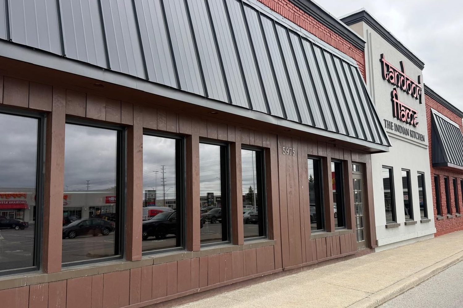 Close view along the side of the Tandoori Flame restaurant in Mississauga, showing a row of new aluminum windows with dark frames and tinted glass set into brown cladding