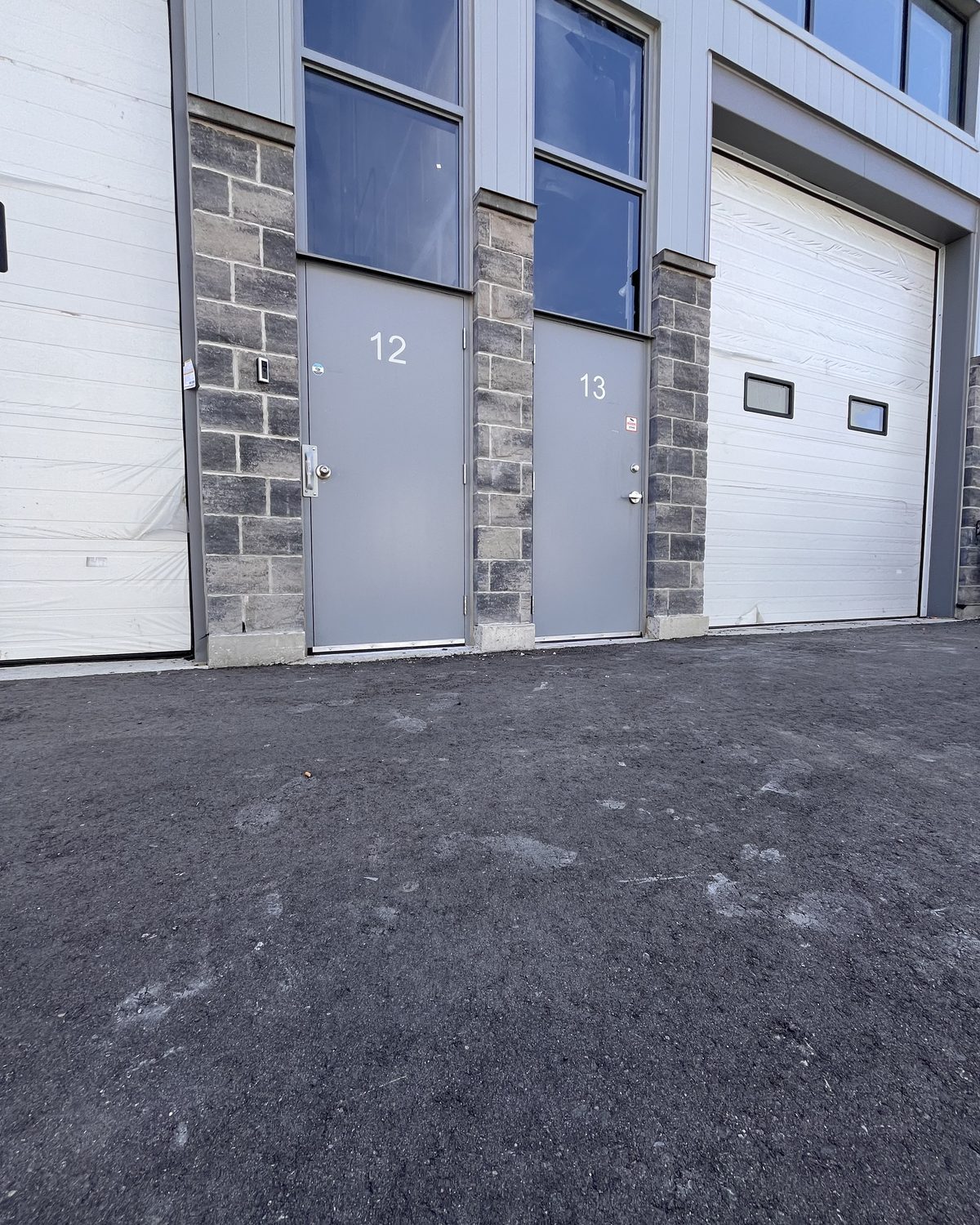 Two grey hollow metal doors with glazed transoms above, side by side in a stone wall between overhead doors, at a warehouse on Solar Drive in Mississauga