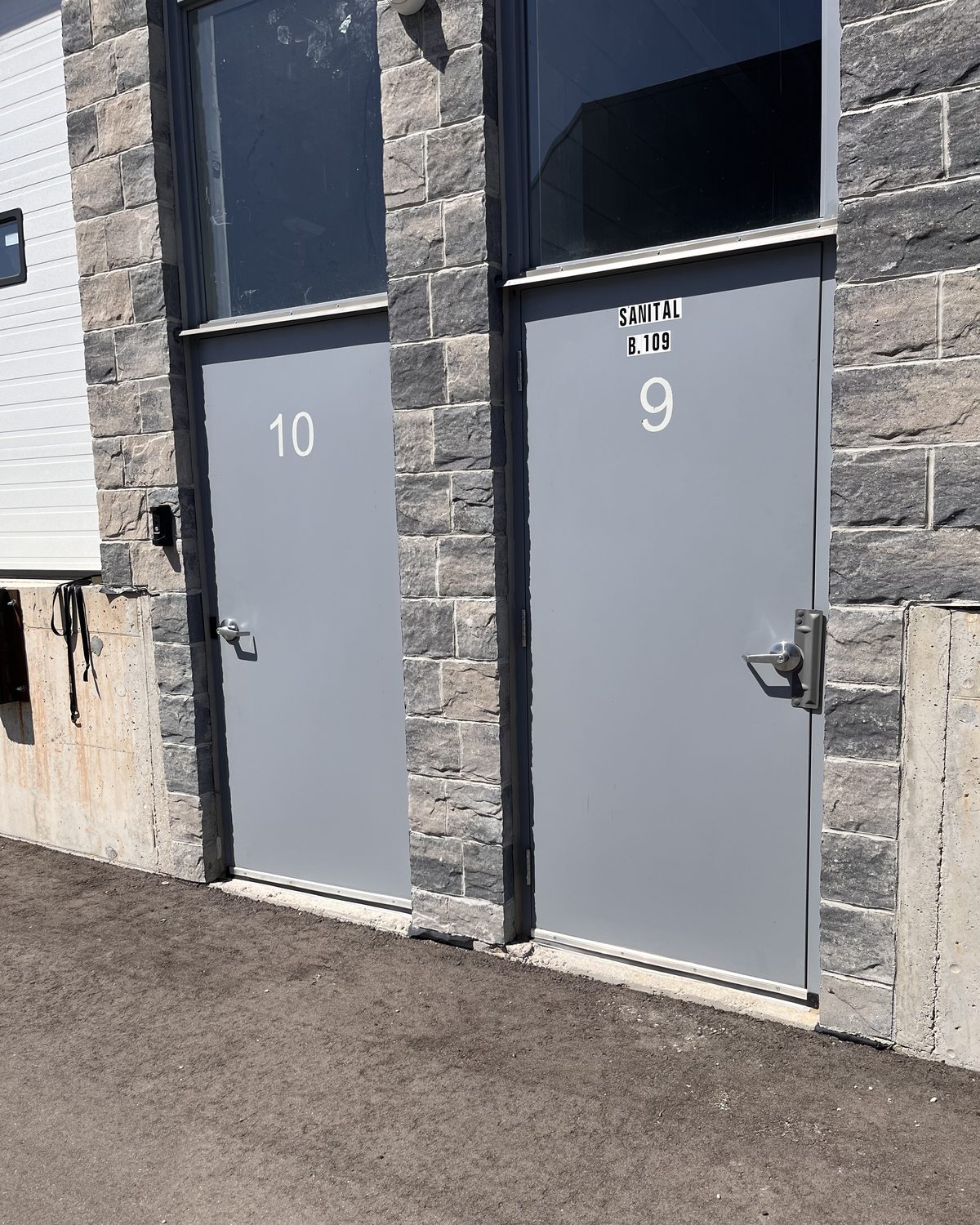 Two numbered grey hollow metal unit doors with tall glazed transoms, set into a stone-faced wall at a warehouse on Solar Drive in Mississauga