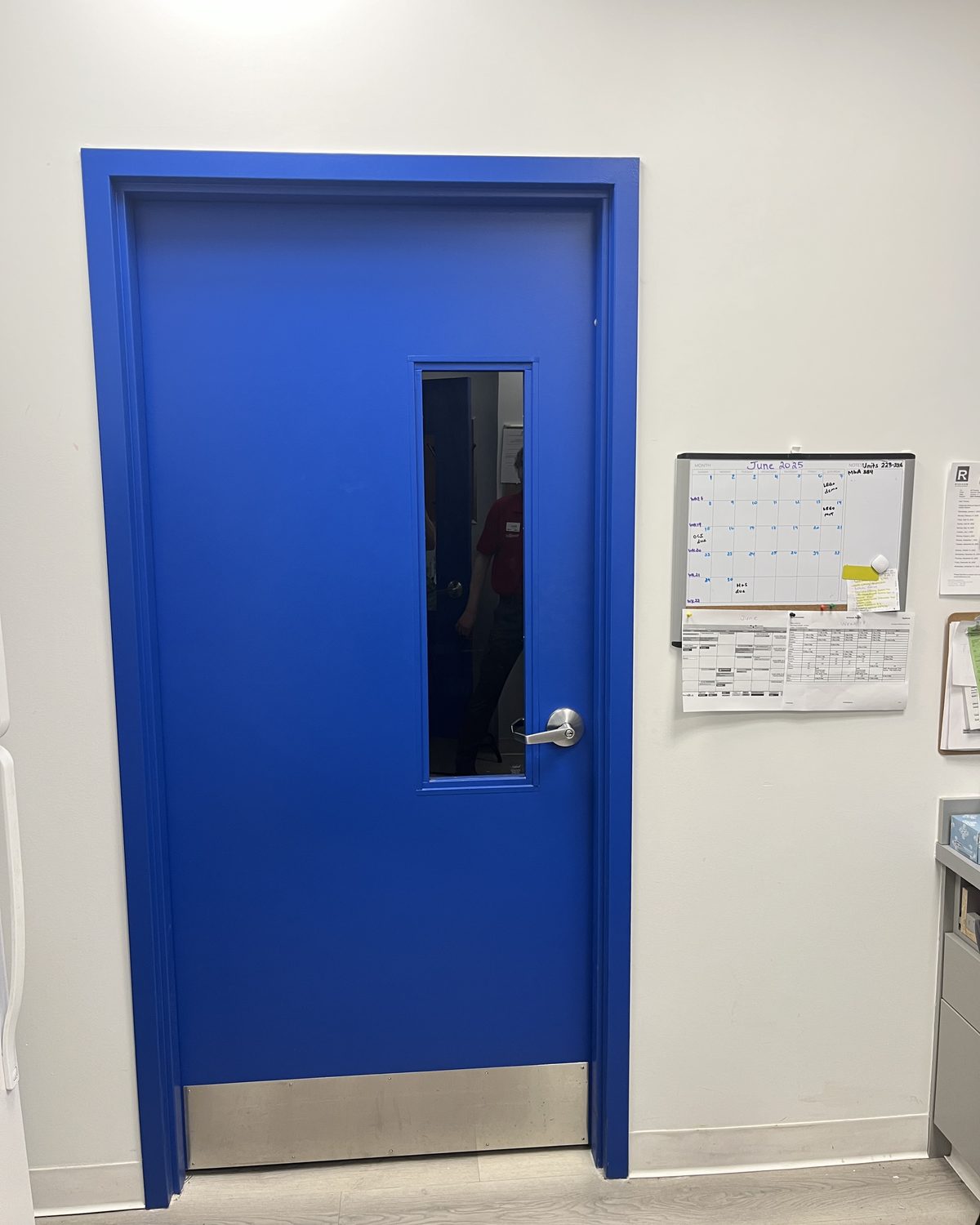 A blue hollow metal door with a narrow vision lite and a stainless kick plate, in a blue frame at a Toys “R” Us store in North York