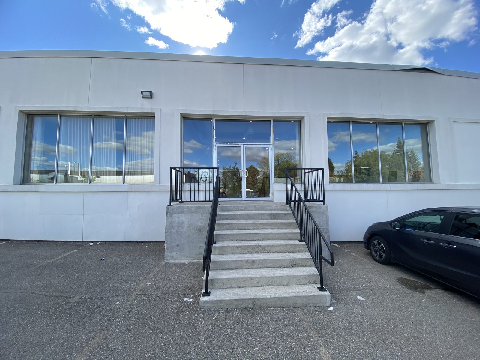 The white-rendered front of the building at 68 Tycos Drive in North York, with a new glazed aluminum entrance at the top of a flight of steps between two wide aluminum windows, installed by Canuck Door Systems