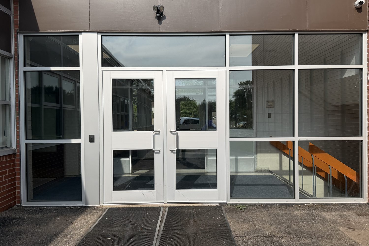 The same aluminum double-door entrance square-on, close enough to read the full-height glazing in each leaf, the transom bar above and the mullion between the pair