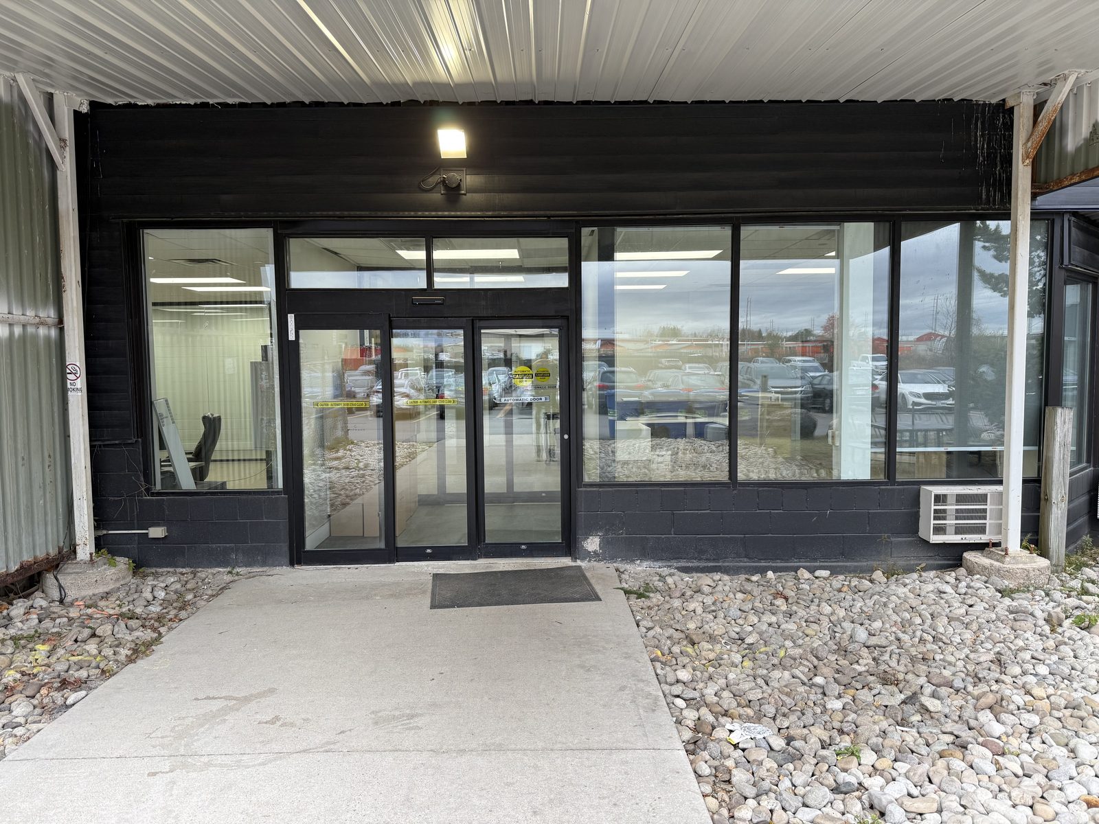 The entrance at 51 Centennial Road in Orangeville under a metal canopy: a pair of automatic sliding glass doors in black anodized framing between wide glazed panels, installed by Canuck Door Systems