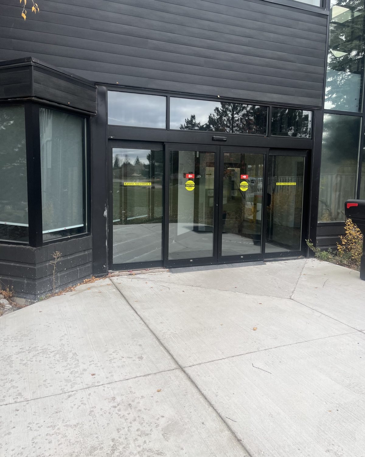 A pair of automatic sliding glass doors in black anodized framing at the entrance of 51 Centennial Road in Orangeville, seen from the paved walkway