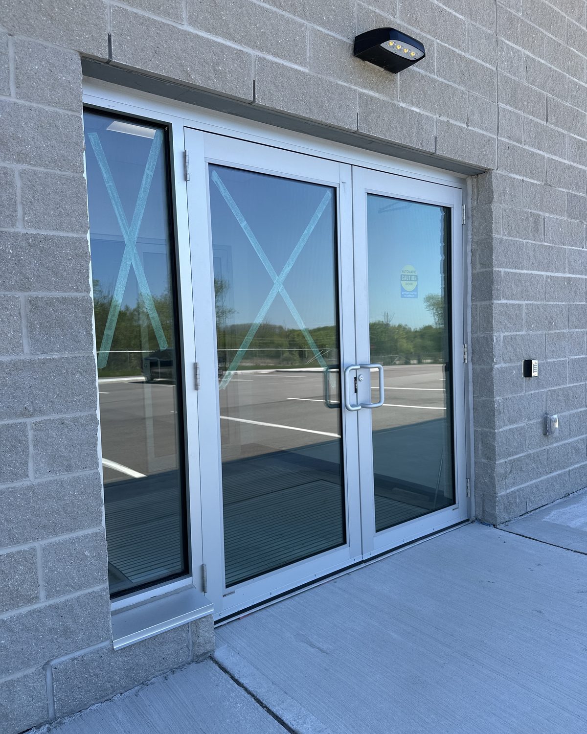 Clear anodized aluminum double doors with a full-height glass sidelite, newly installed in a block-wall entrance