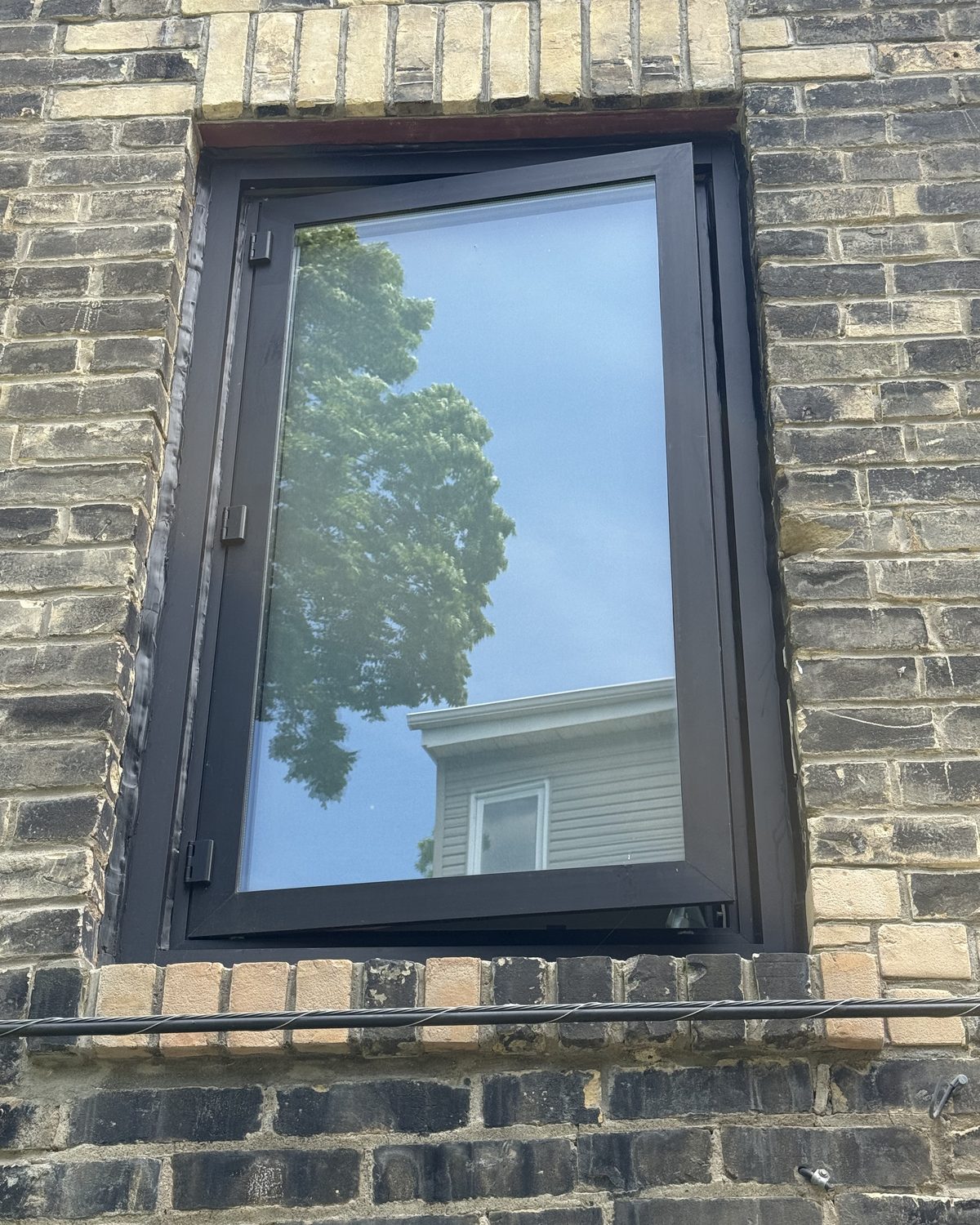 A new black anodized aluminum casement window set into an older yellow brick wall on the upper floor of a Scarborough building