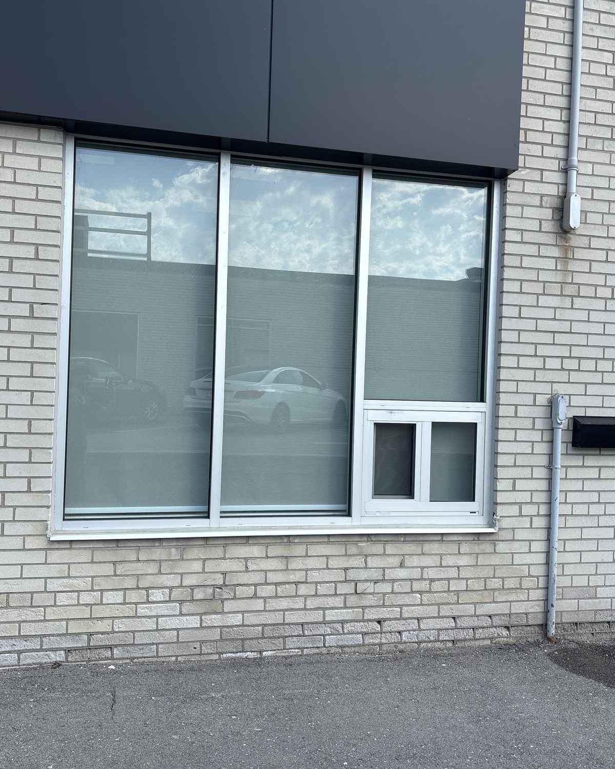 A large aluminum-framed window in the light brick wall of a commercial building in Scarborough, with a smaller opening unit set into its lower corner