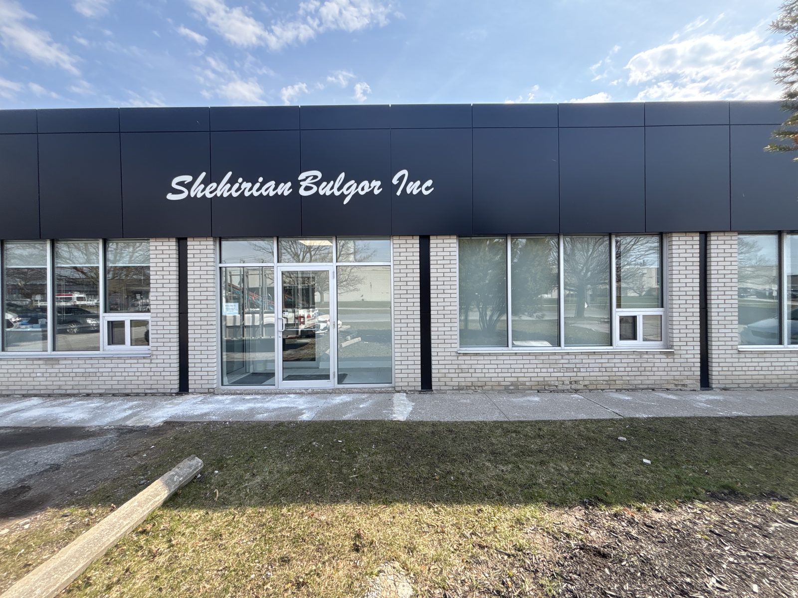The front of a single-storey commercial building in Scarborough with a dark fascia band above a row of new aluminum storefront windows and a glazed entrance set into light brick, installed by Canuck Door Systems