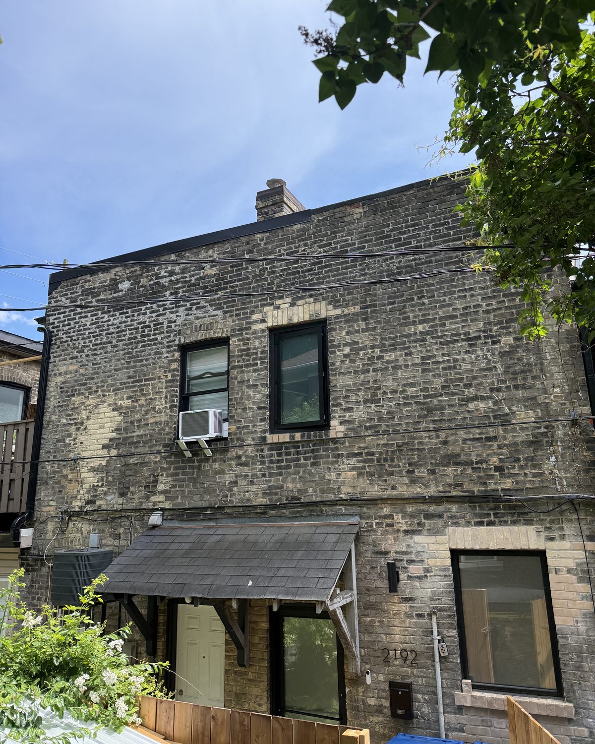 The rear of an older yellow brick building in Scarborough with new black-framed aluminum windows on both floors
