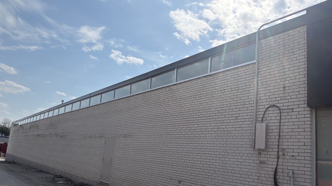 The long light brick side wall of the warehouse in Scarborough, with a continuous band of new high-level windows running along the top of the wall under the roof line